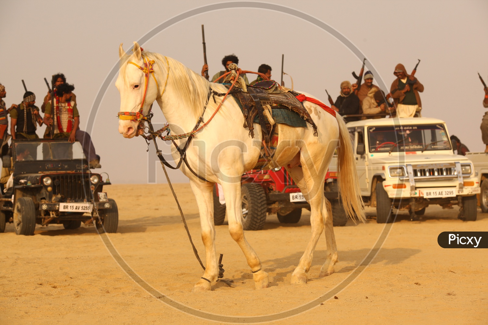 A horse and the people with guns on the vehicles in the desert