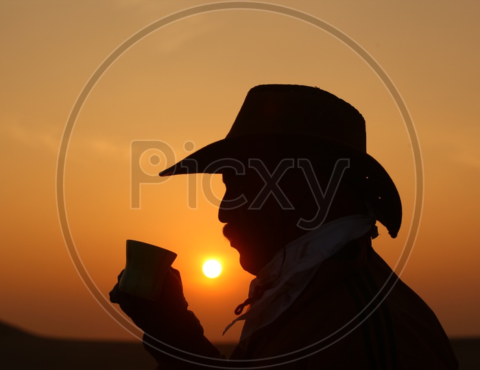 silhouette of a person with a cowboy hat and a cup in the hand