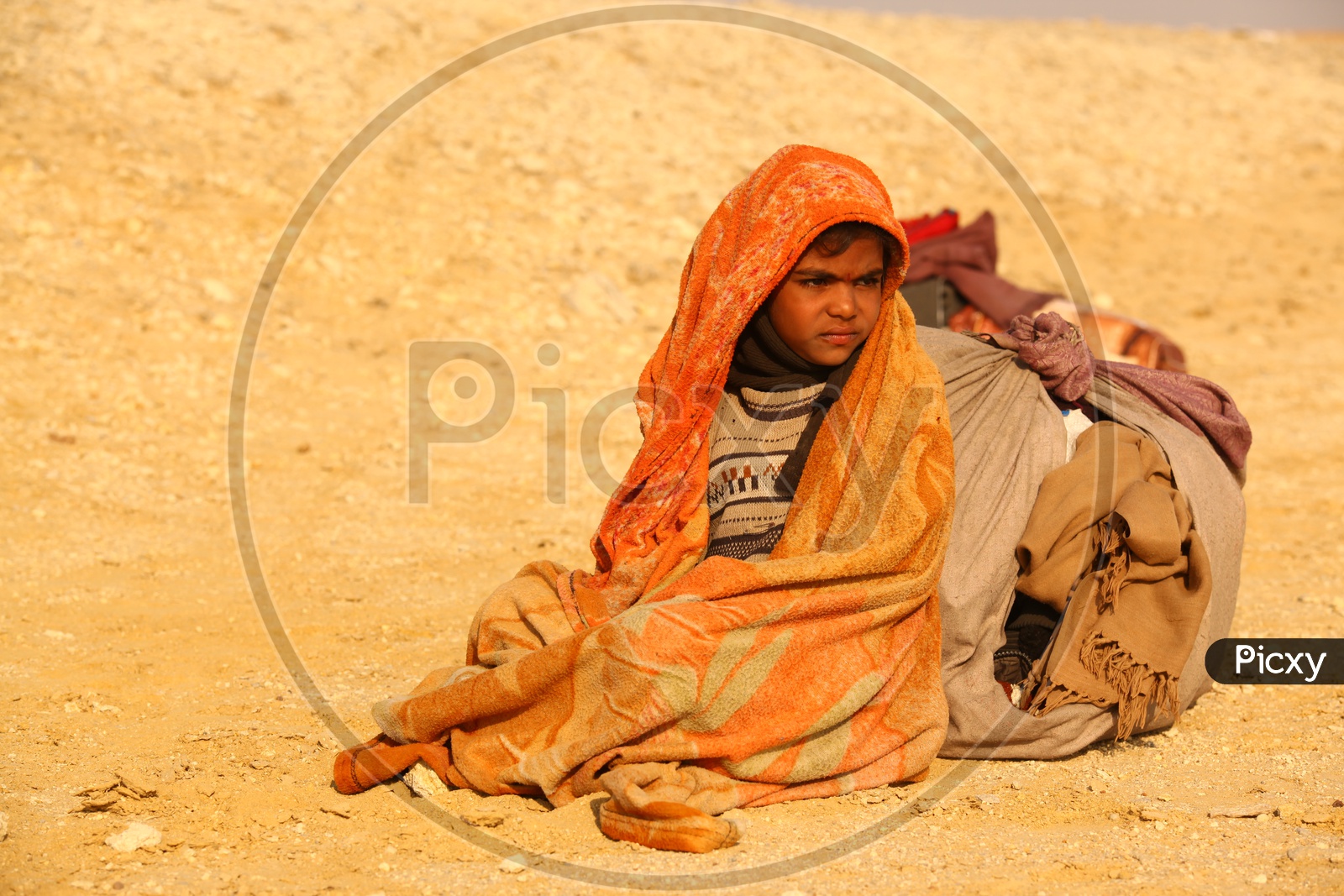 A kid covered with blanket in the desert