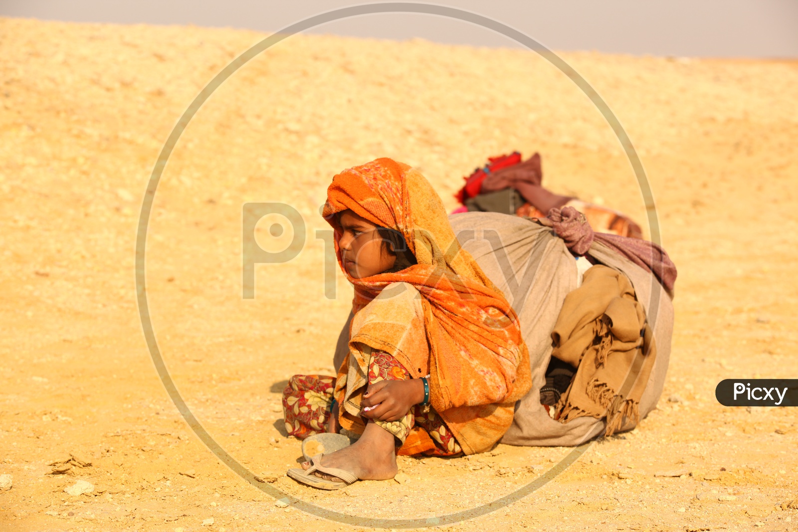 Child covered with blanket seated in the desert