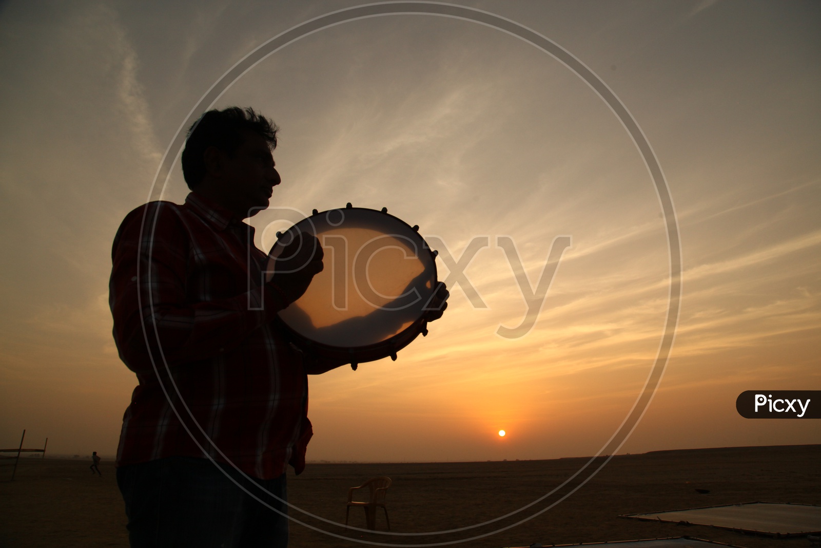 Silhouette of a person playing drums and sunset in the background