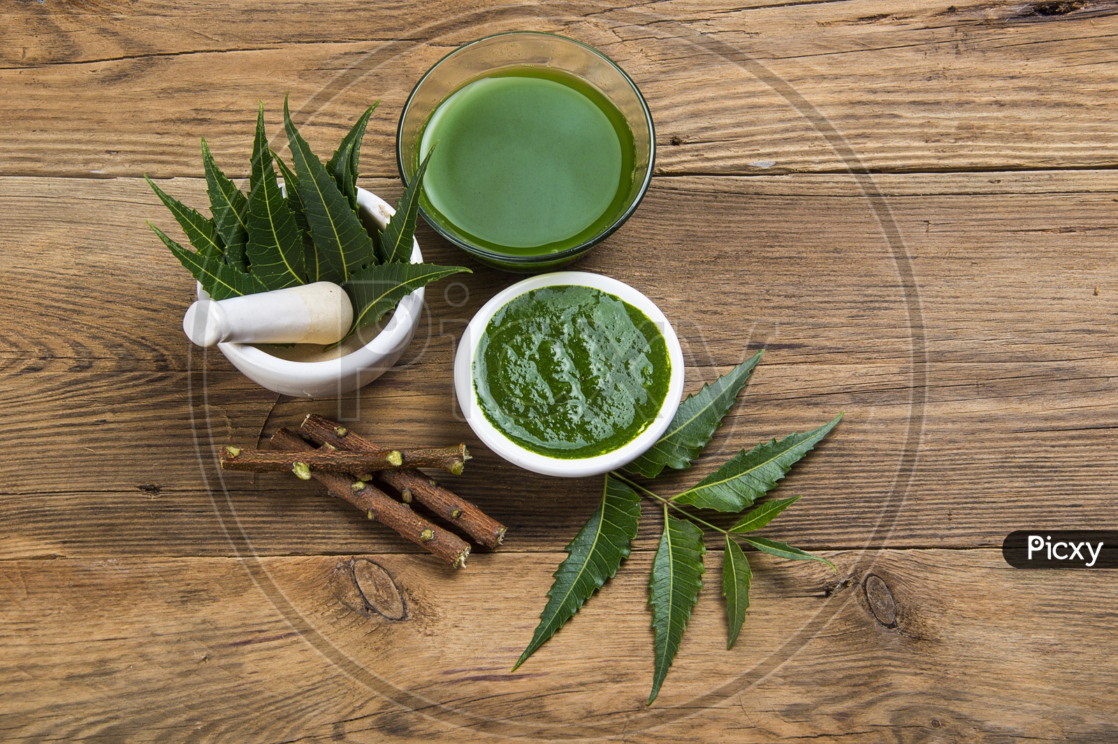 Medicinal Neem leaves in mortar and pestle with neem paste, juice and twigs on wooden background