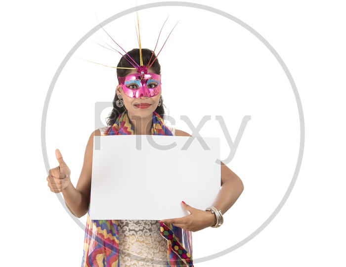 A Happy Young Indian Girl Wearing Carnival Mask And Holding White Board or Placard