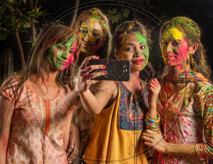 A Group Of Young Girls Filled In Holi Colors and Taking A Selfie In Smart Phone
