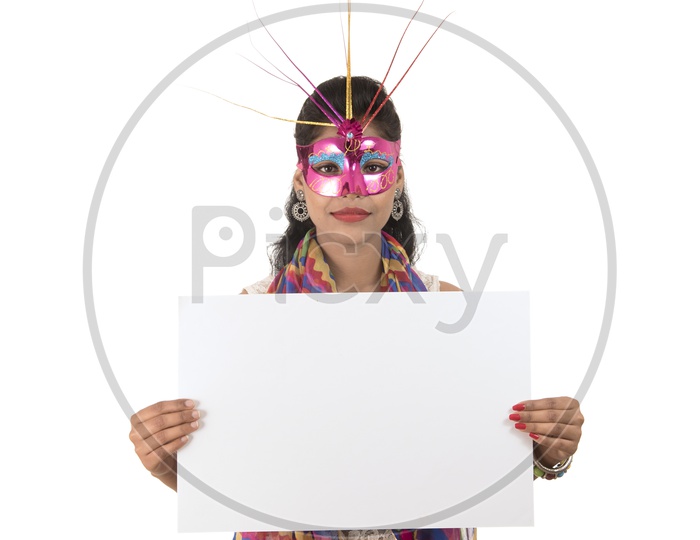 A Happy Young Indian Girl Wearing Carnival Mask And Holding White Board or Placard