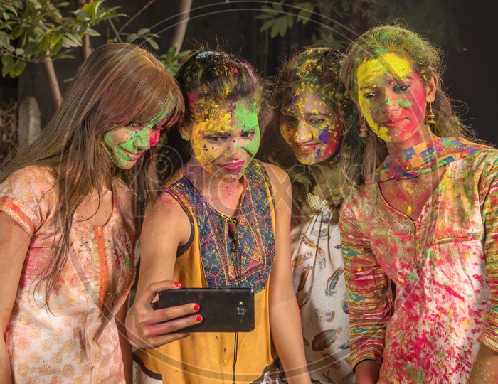 A Group Of Young Girls Filled In Holi Colors and Taking A Selfie In Smart Phone
