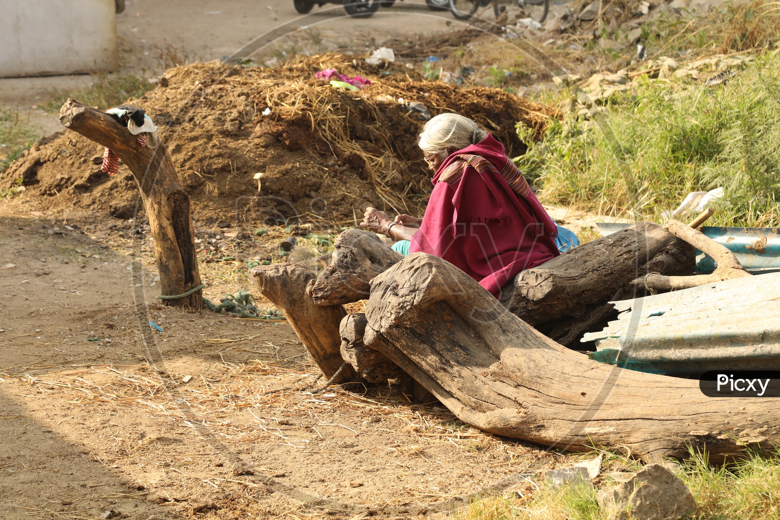 An old woman sitting near a log of wood