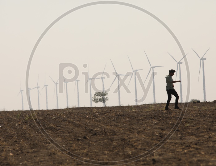 A man Walking Alone On Barren Lands With Wind mills In Background