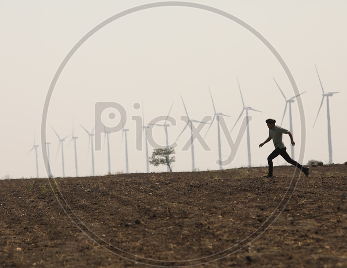 A Man Running in Barren Land With Wind Mills In Background