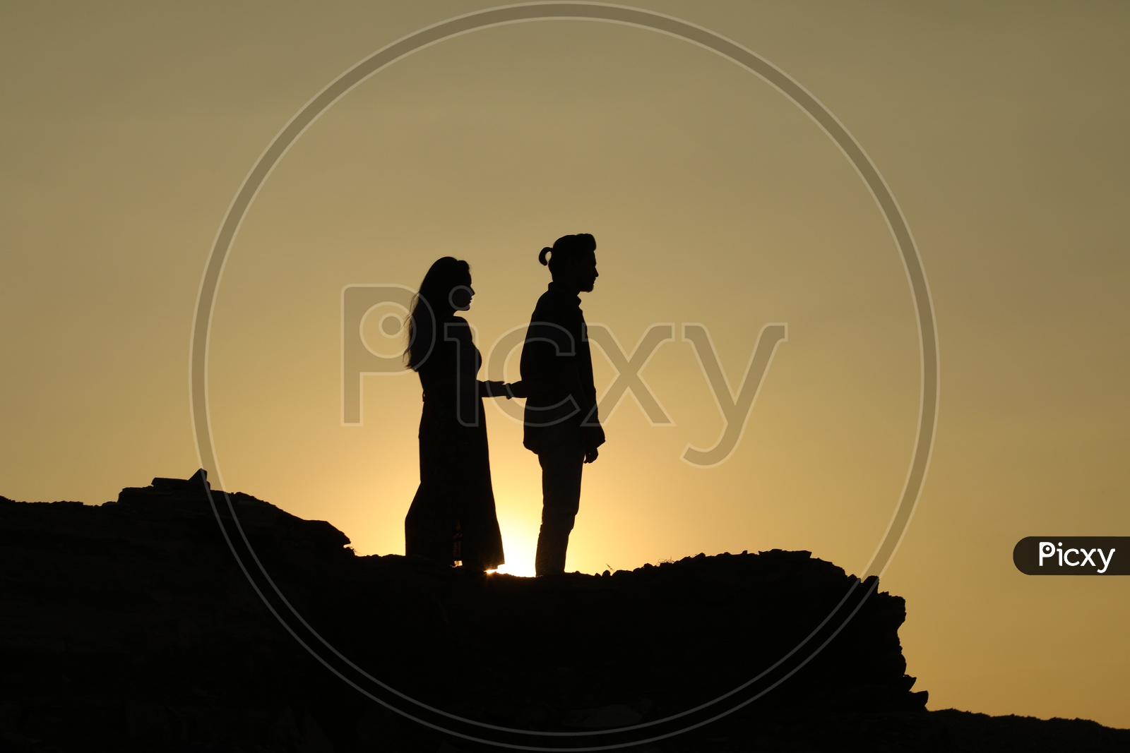 Silhouette of man and woman on top of the rocky hill