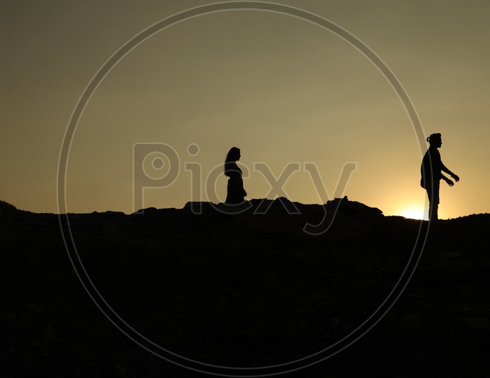 Silhouette of man and woman walking on the top of the rocky hill