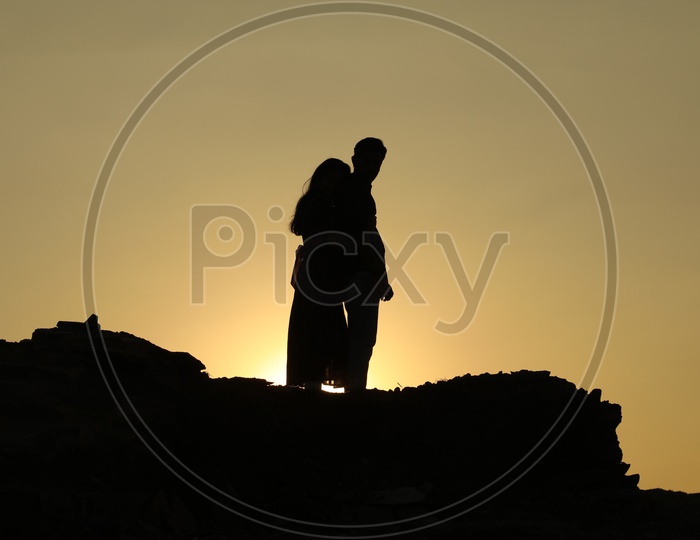 Silhouette of a woman hugging a man from behind on the top of the rocky hill