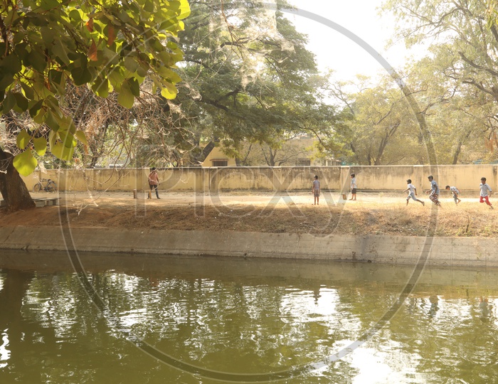 Children playing cricket beside a water canal
