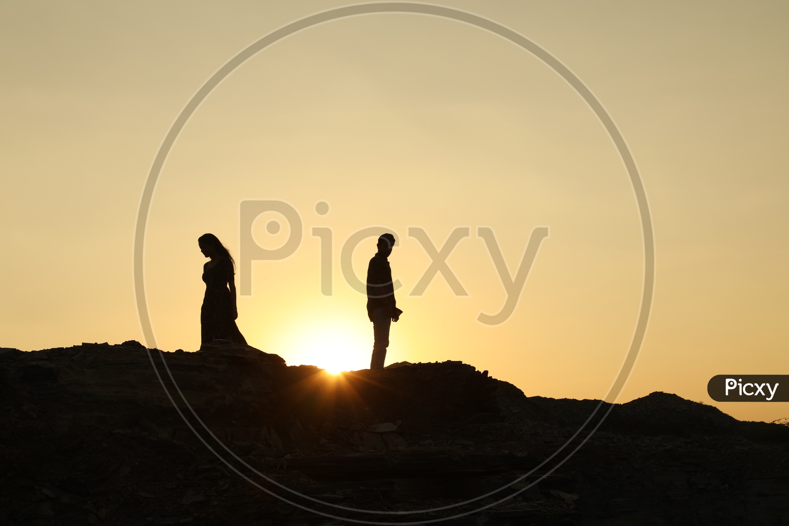 Silhouette of man and woman walking in the opposite direction on the top of the rocky hill