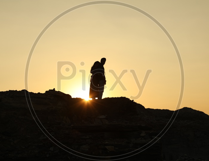 Silhouette of a woman hugging a man from behind on top of the rocky hill