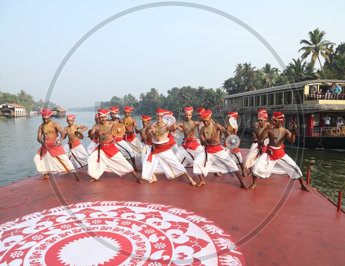 A Group Of Dancers In Kerala Traditional Dancers Attire Dancing On a Boat With Kerala Backwaters Background