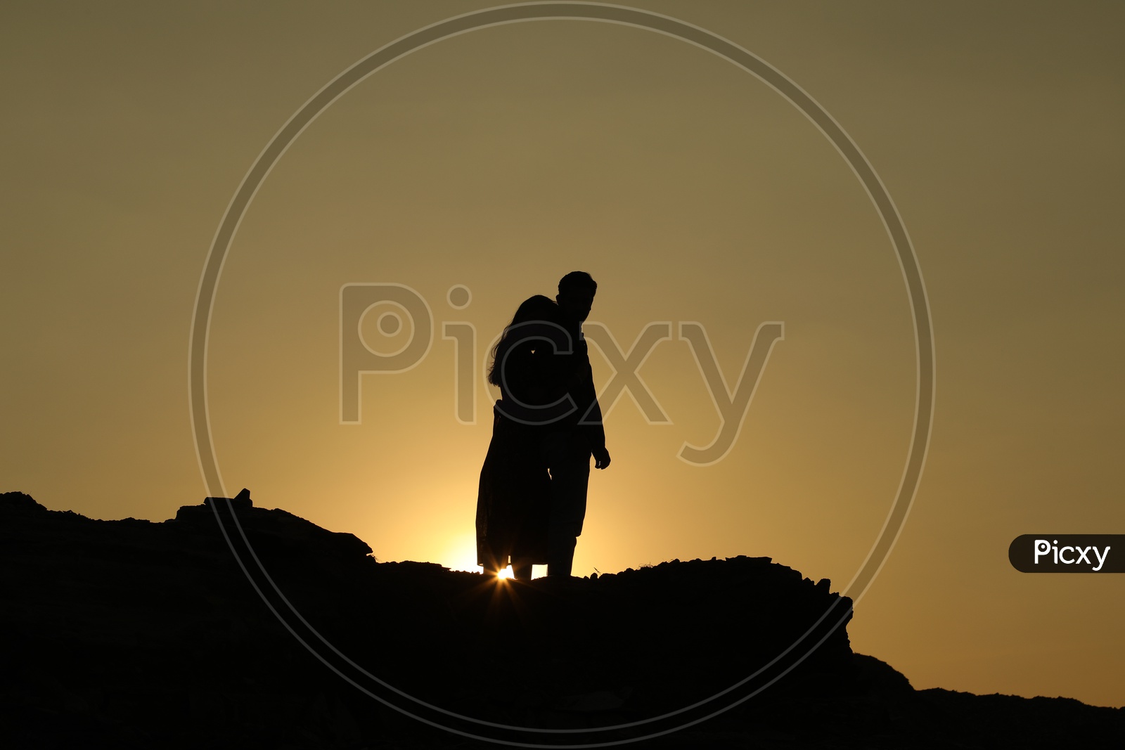Silhouette of a woman hugging a man from behind on top of the rocky hill