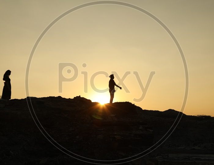 Silhouette of man and woman walking on the top of the rocky hill