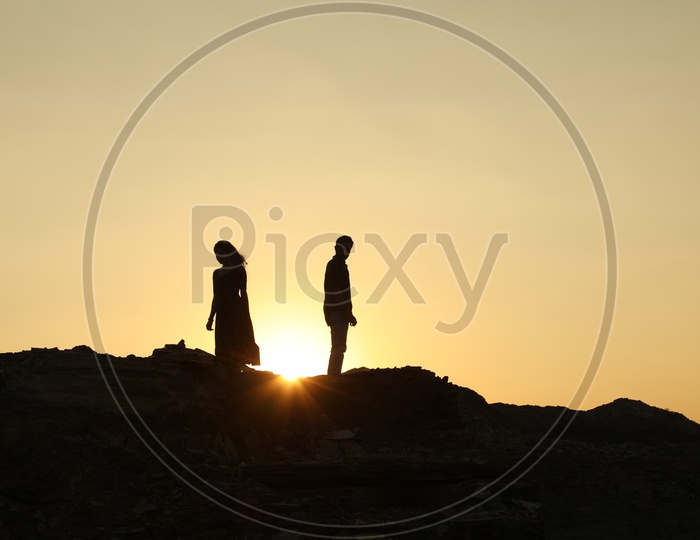 Silhouette of man and woman walking in the opposite direction on the top of the rocky hill