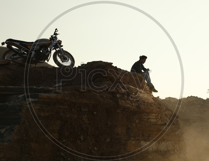Silhouette of man and a bike on the top of the rocky hill