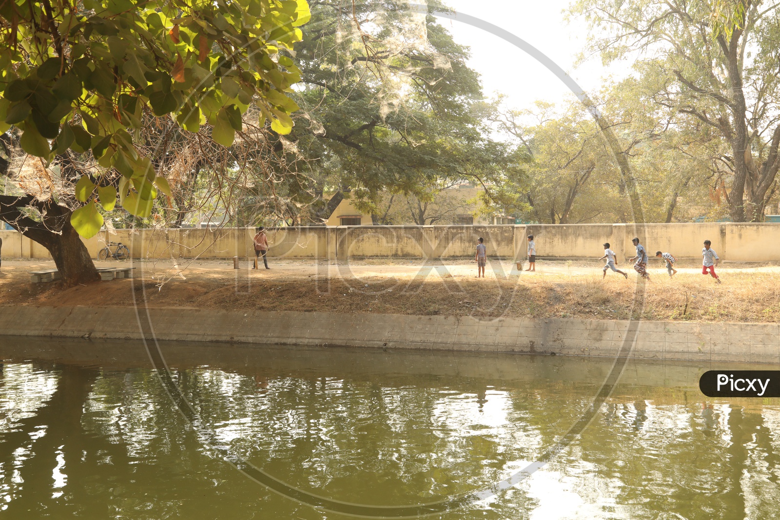 Children playing cricket beside a water canal
