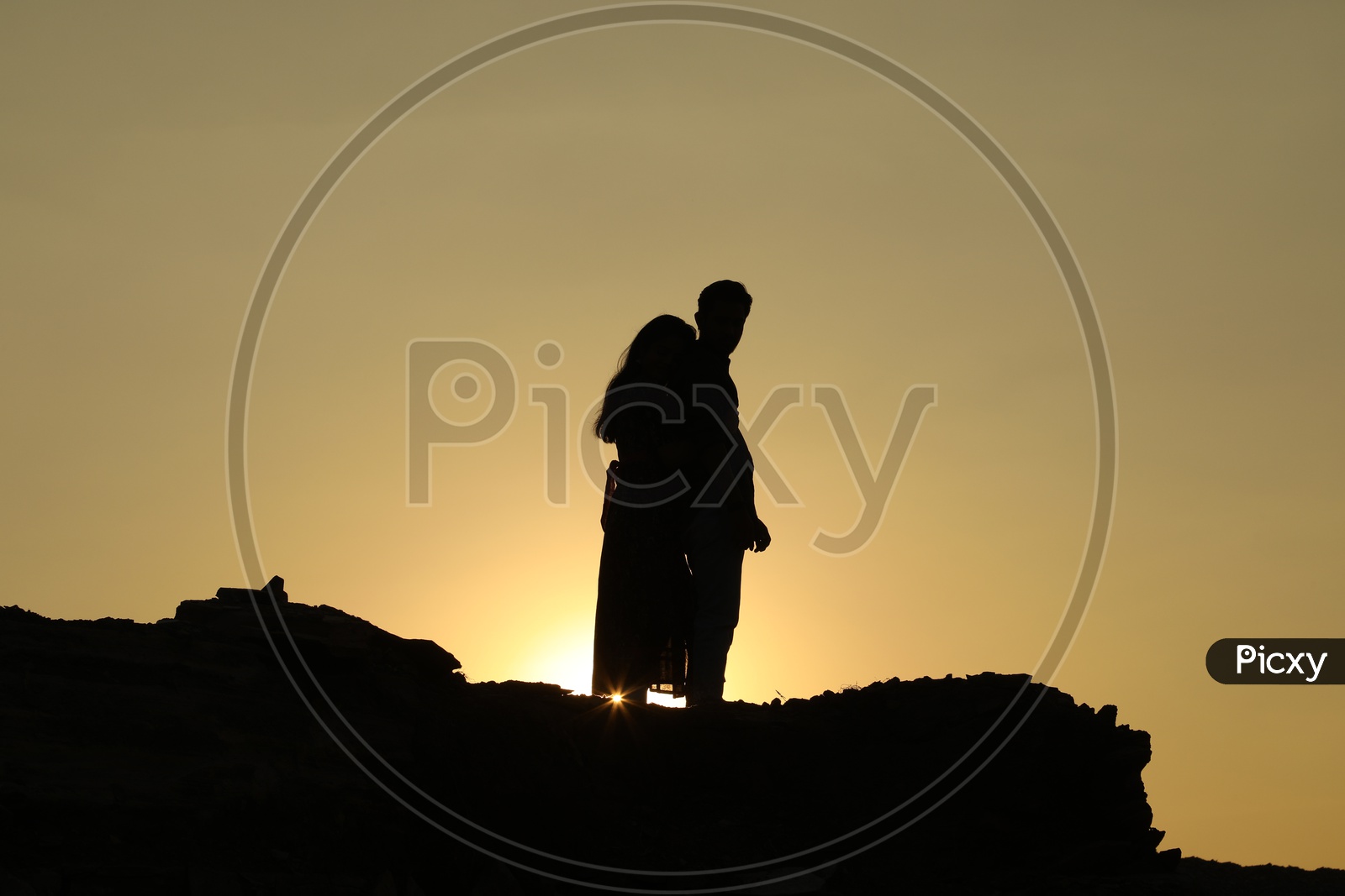 Silhouette of a woman hugging a man from behind on the top of the rocky hill