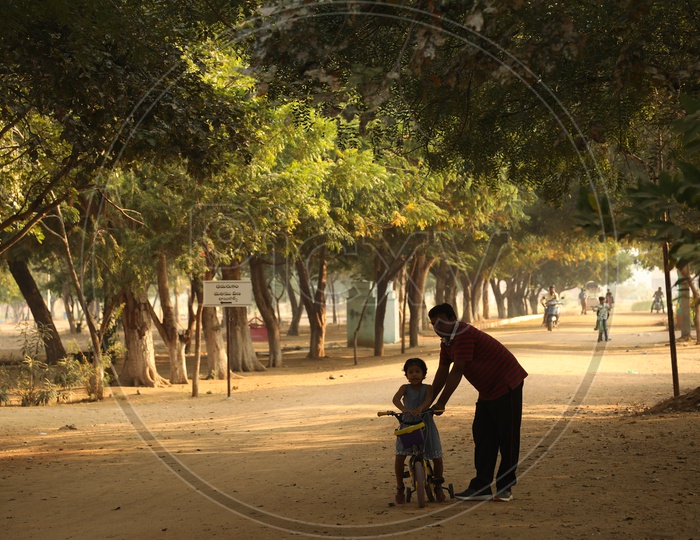 A father helping his daughter with the cycle in the play ground