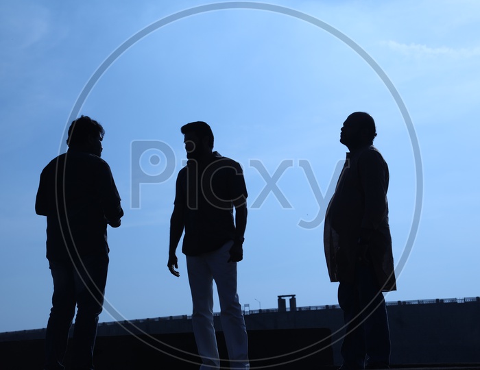Silhouette of three men talking along the bridge side