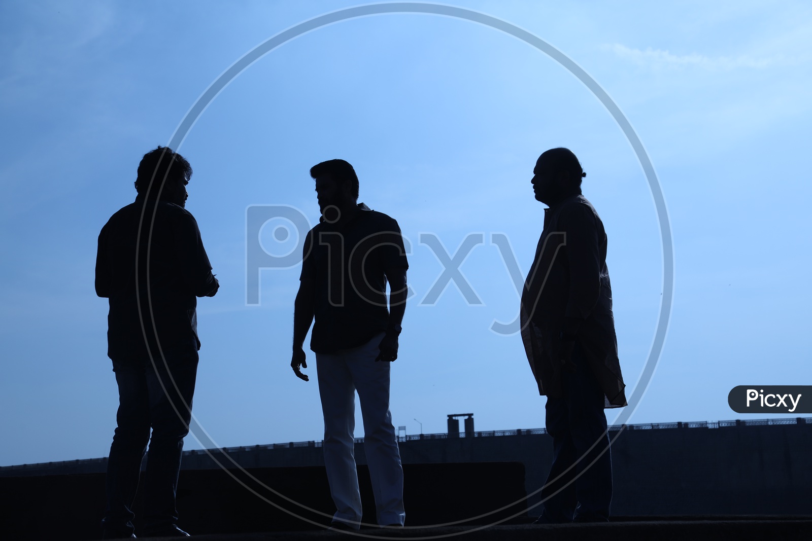 Silhouette of three men talking along the bridge side