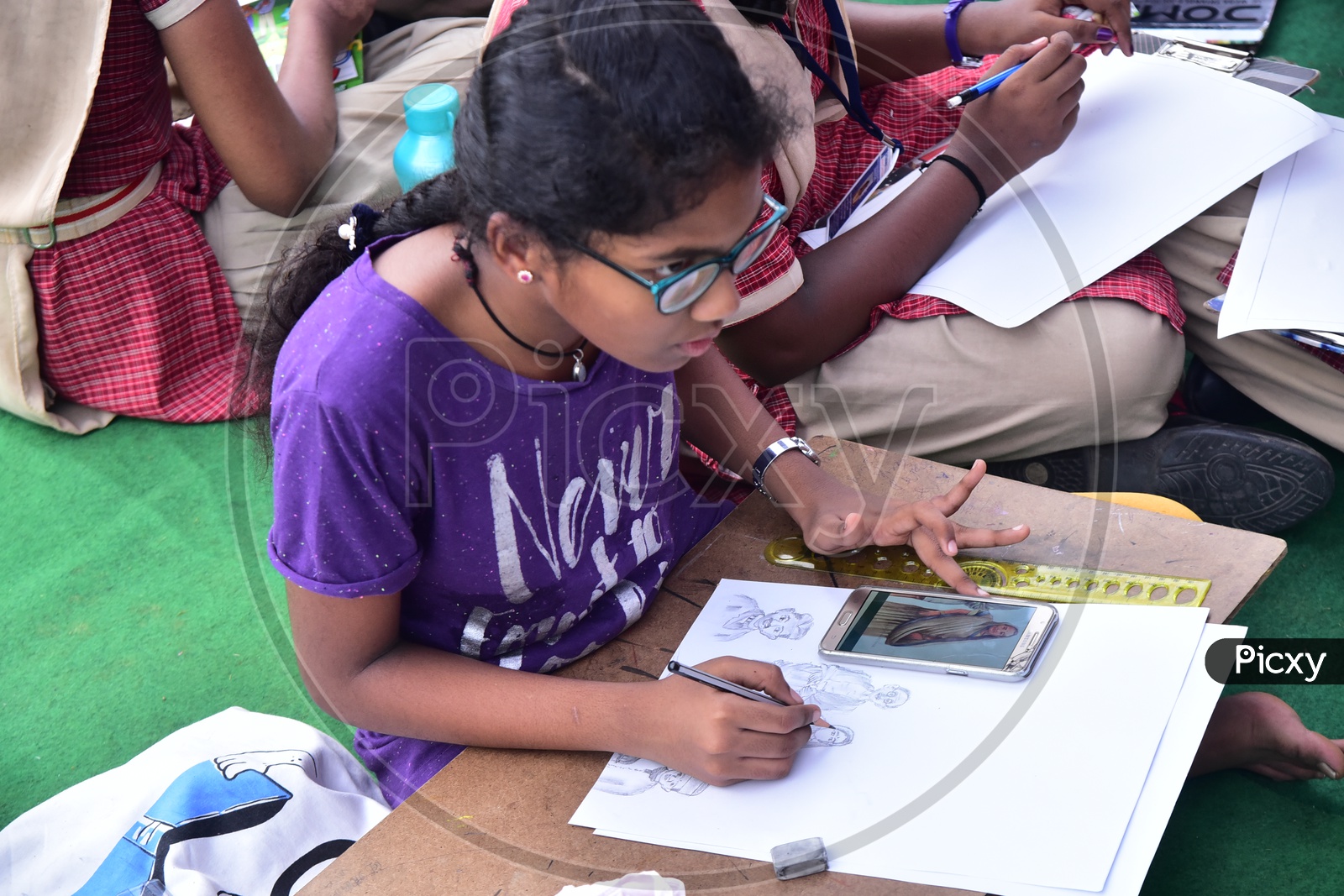A school girl drawing a sketch with the help of cellphone during a competition