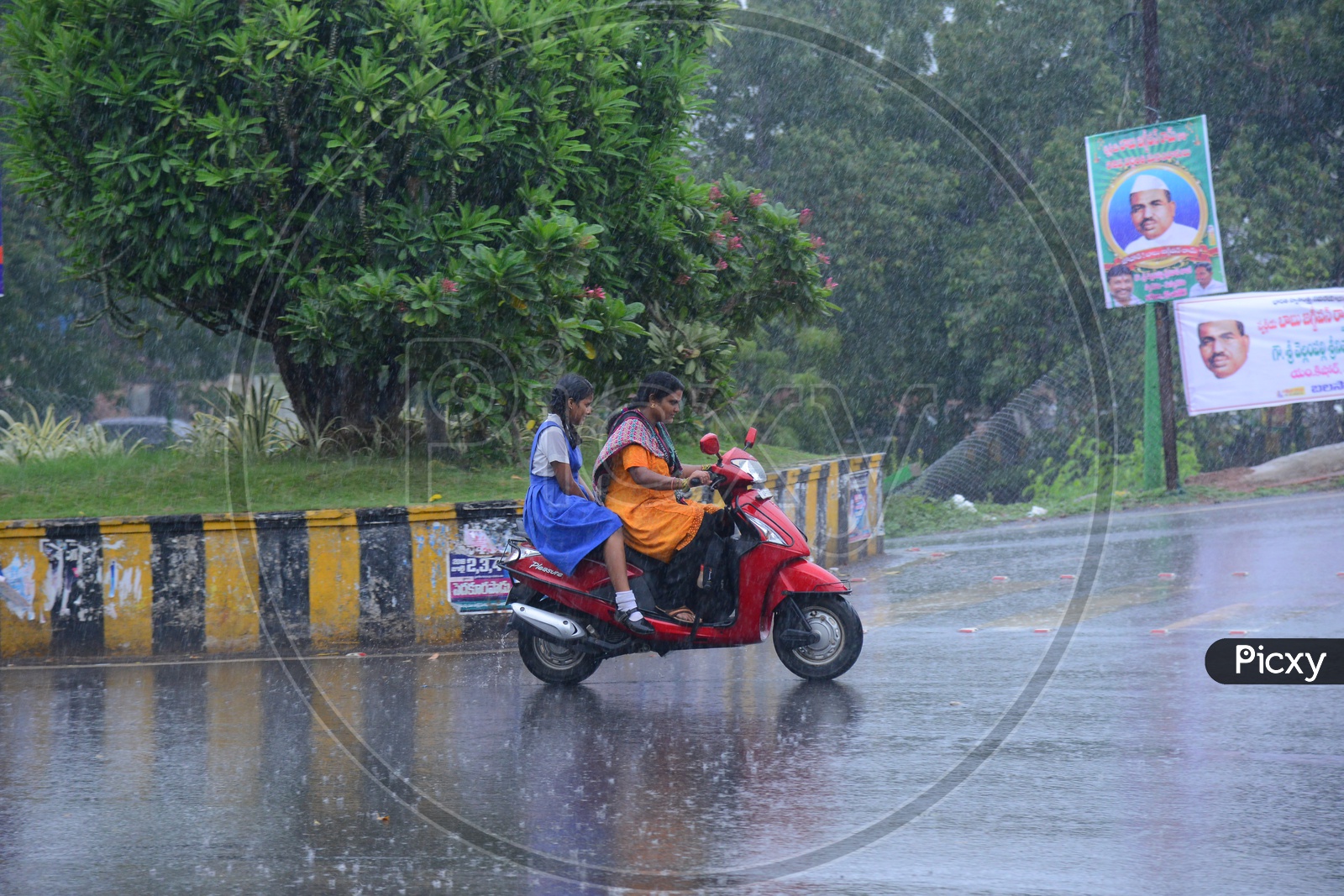 A woman riding a bike with girl behind on the road while its raining