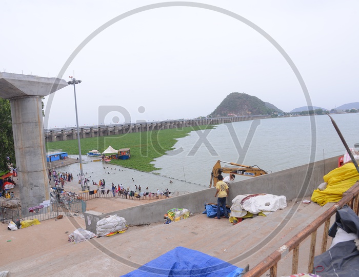 A View Of  People Bathing In Krishna River Water with Prakasham Barrage In Background