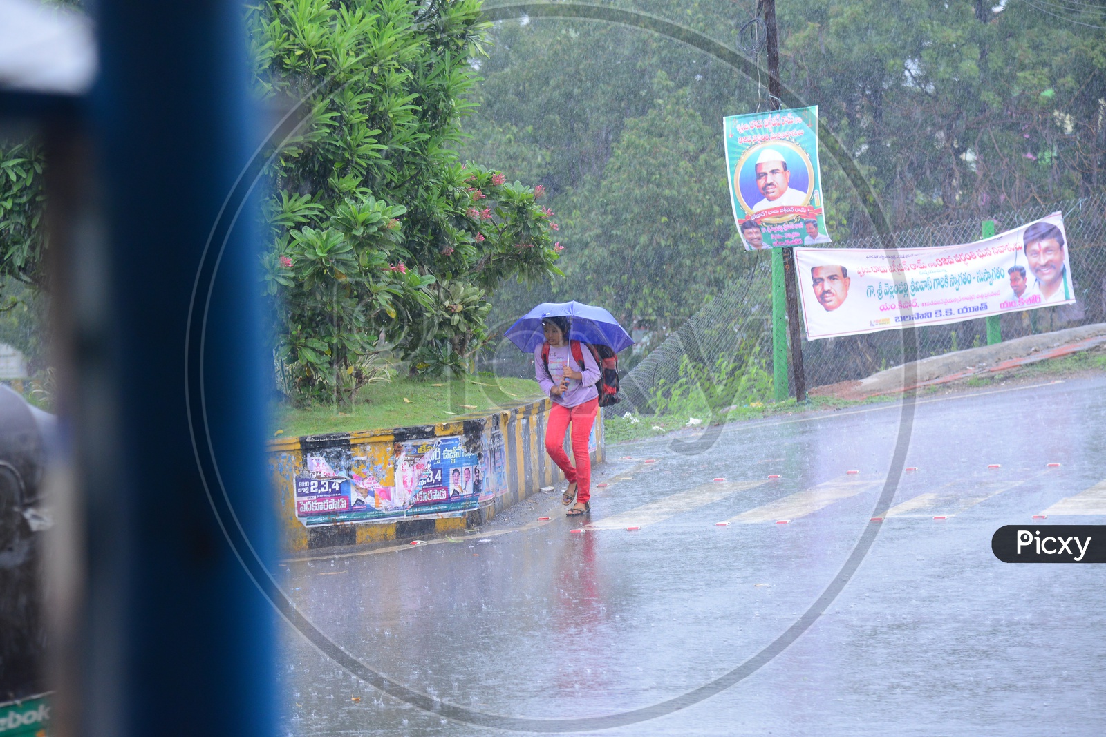 A girl walking with an umbrella on the road while its raining