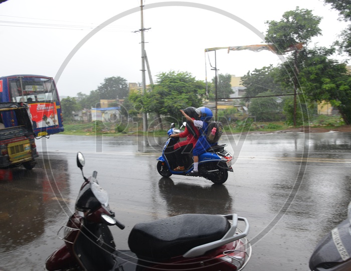A mother and daughter going on a scooty on road in rain