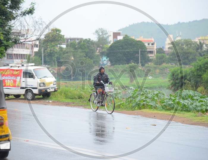 A woman wearing a raincoat and riding a bicycle on road during rain