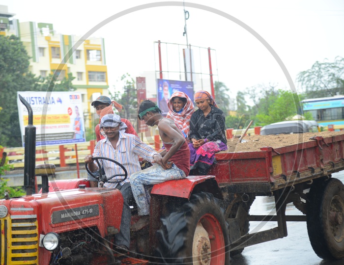 A moving tractor with sand trolley on road during rain