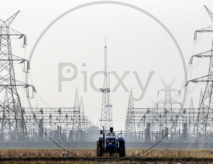 A farmer ploughing the field, electrical substation in the background