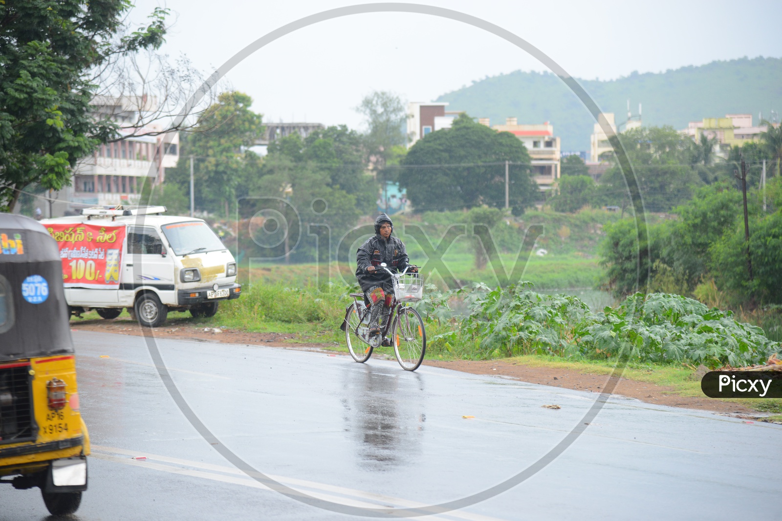A woman wearing a raincoat and riding a bicycle on road during rain