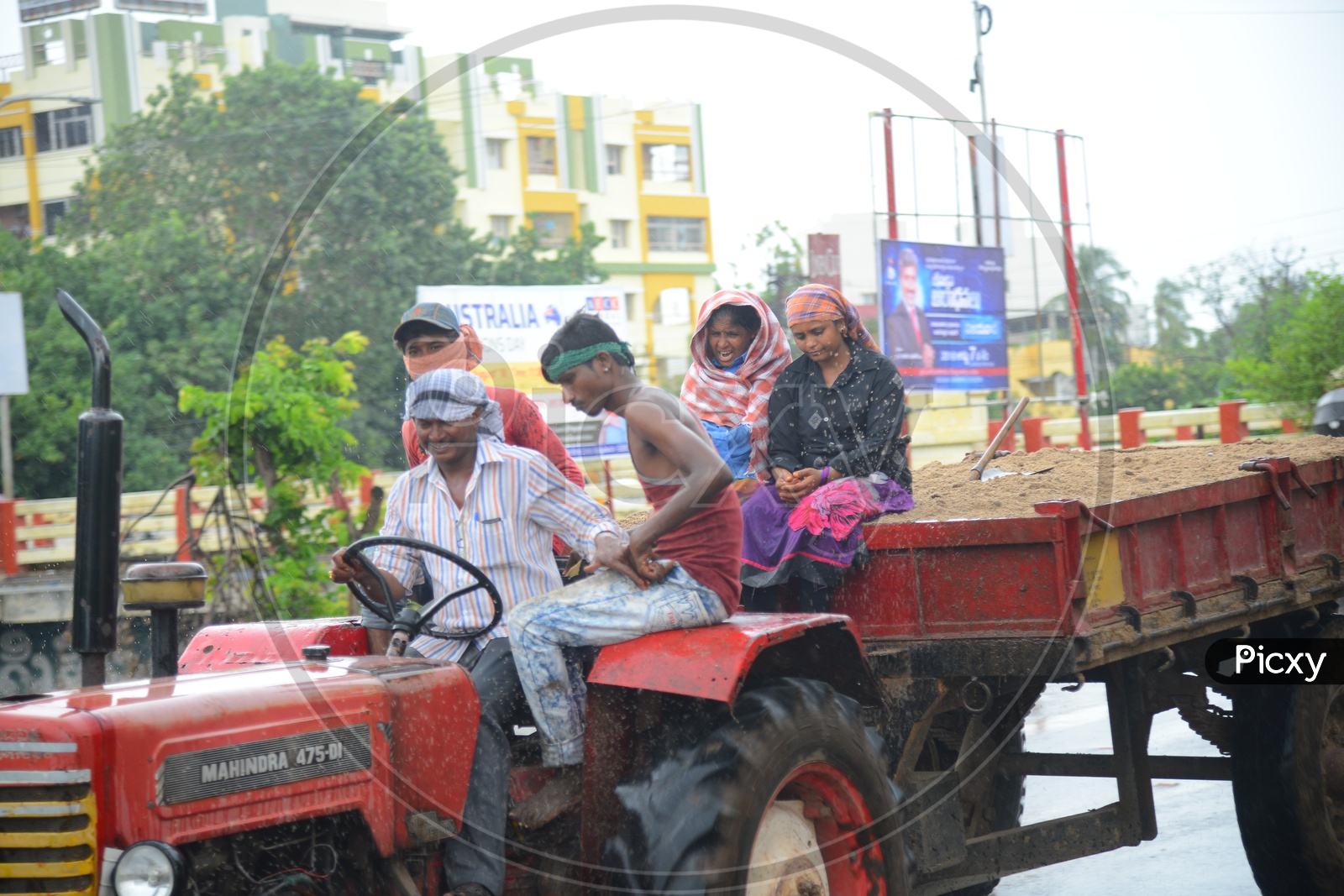 A tractor with sand trolley on road during rain