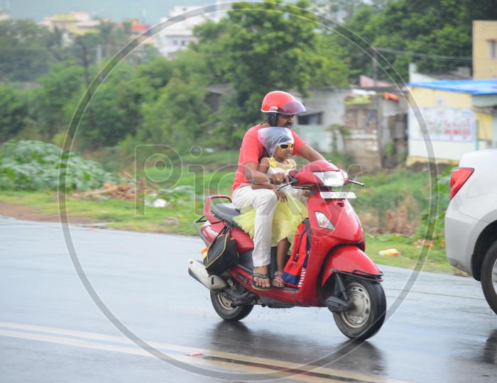 A father and daughter going on a red scooty on road during rain