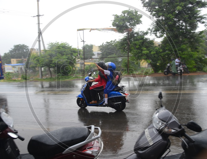 A mother and daughter going on a scooty on road in rain