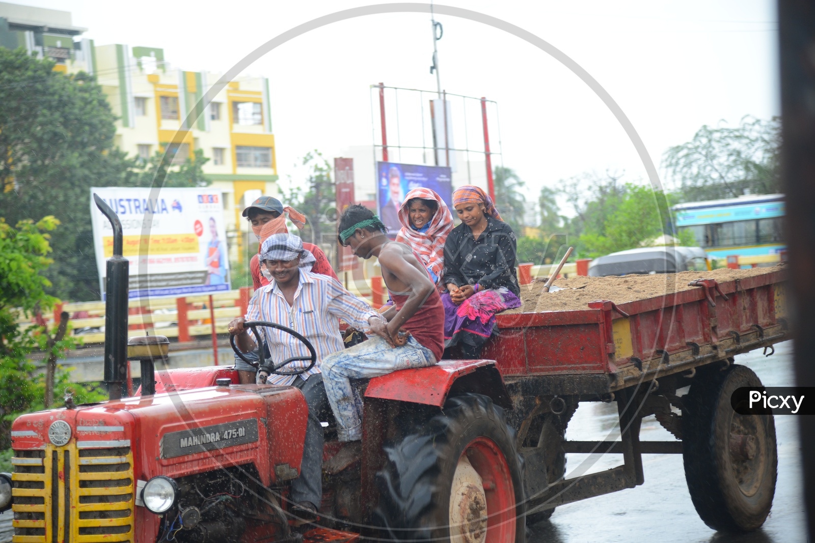 A moving tractor with sand trolley on road during rain