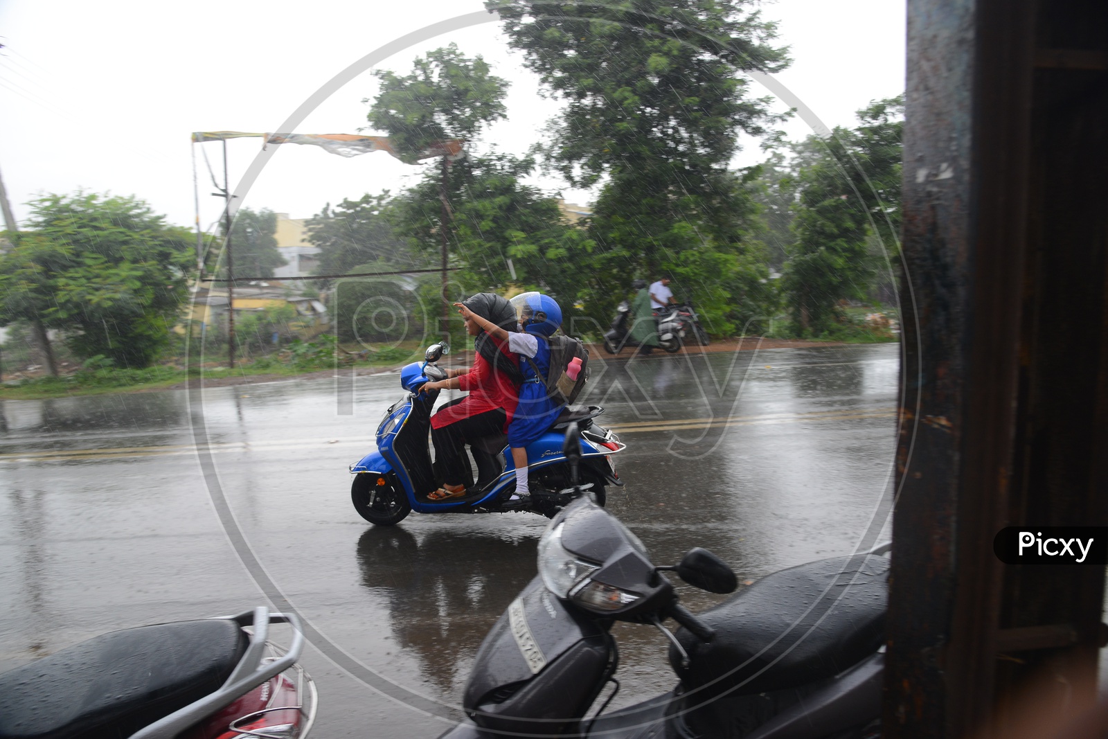 Mother and her daughter going on a Scooty on road during rain