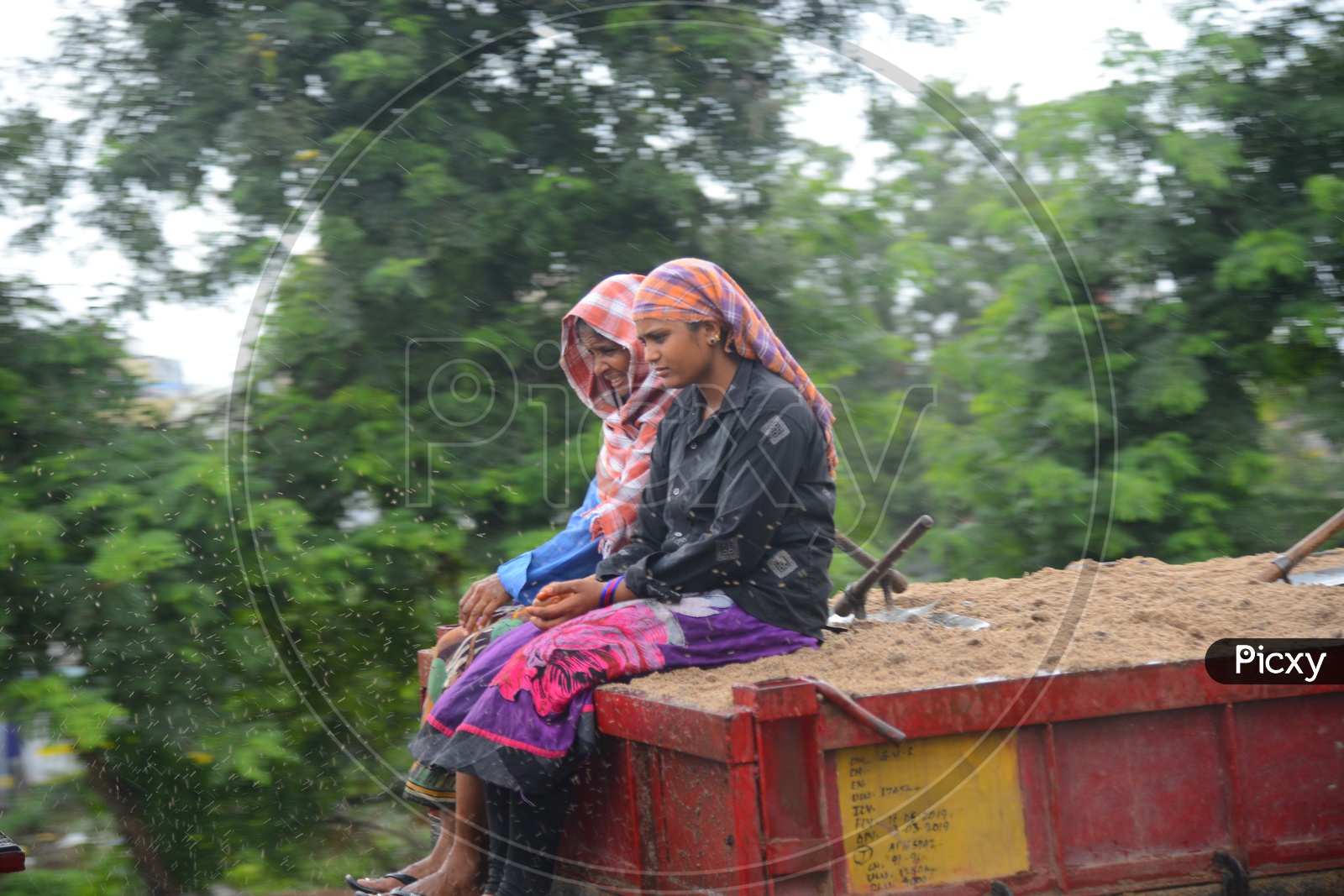 Women Workers sitting on a tractor trolley with sand on a rainy day