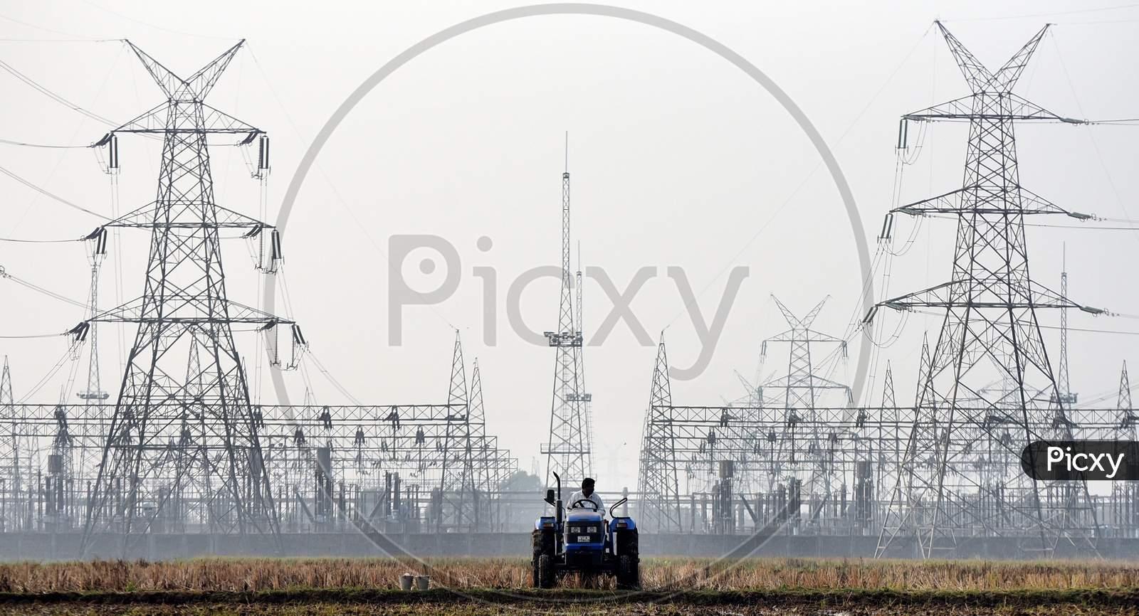 A farmer ploughing the field, electrical substation in the background