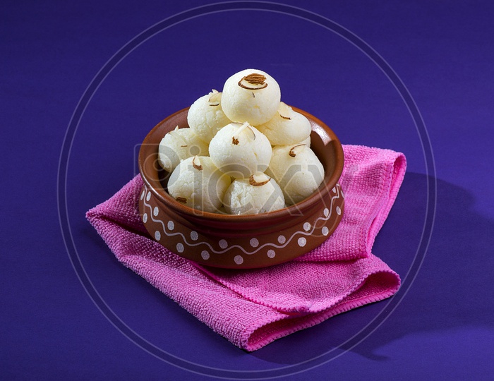 Rasgulla in a clay bowl with napkin on violet background