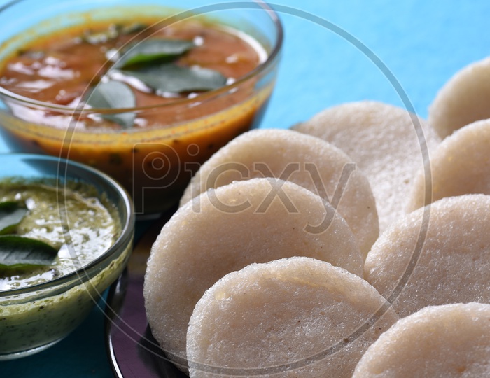 Idli served with sambar and coconut chutney on blue background