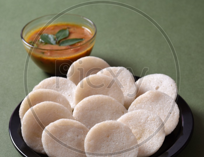 Idli served with sambar and coconut chutney on green background