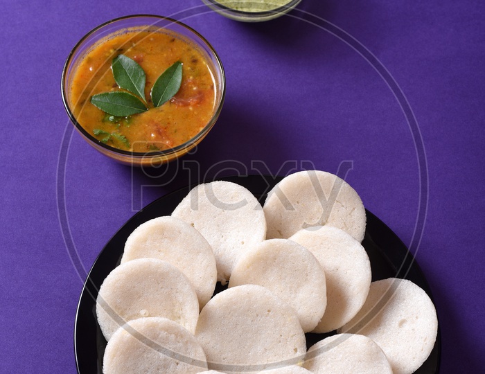 Idli with sambar and coconut chutney on violet background