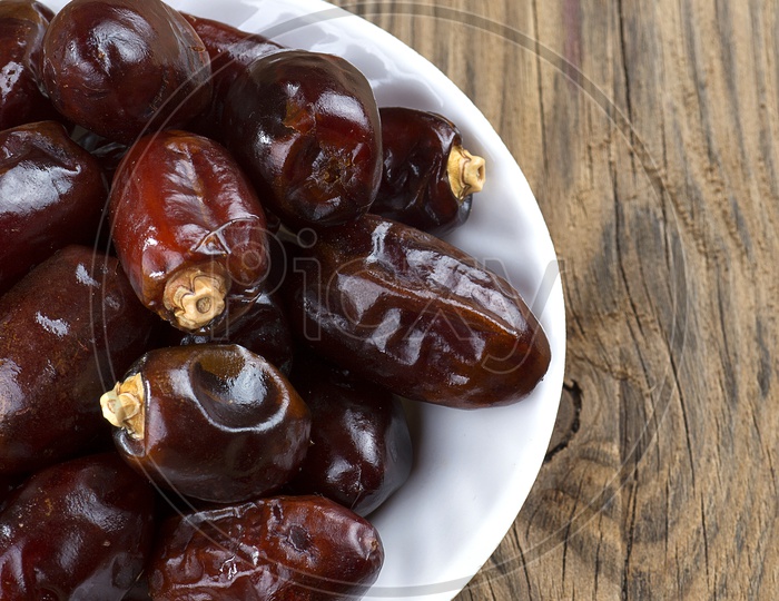 Dates in a white bowl on wooden backdrop